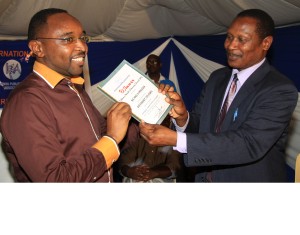 Ng'ang'a Mbugua (Left), is all smiles as he receives his winner's certificate from Prof Egara Kabaji, who was the chief guest at the ceremony
